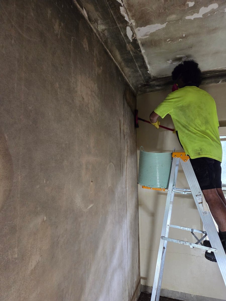 CleanUp Partners technician in full PPE respirator and Tyvek suit scrubbing heavy black mould off walls